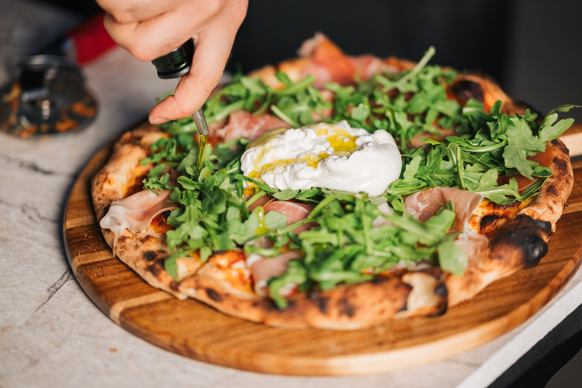 Pizza with prosciutto, burrata and arugula finished with olive oil