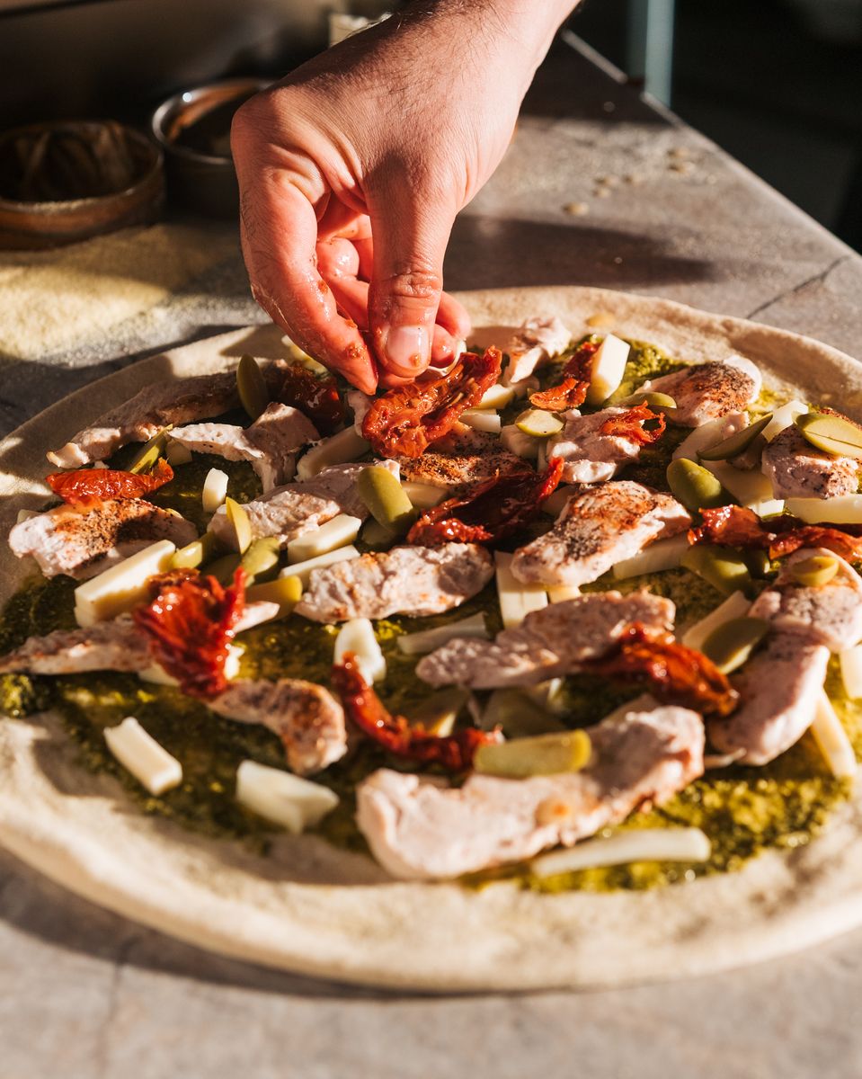 Hand-stretched dough being topped with fresh ingredients