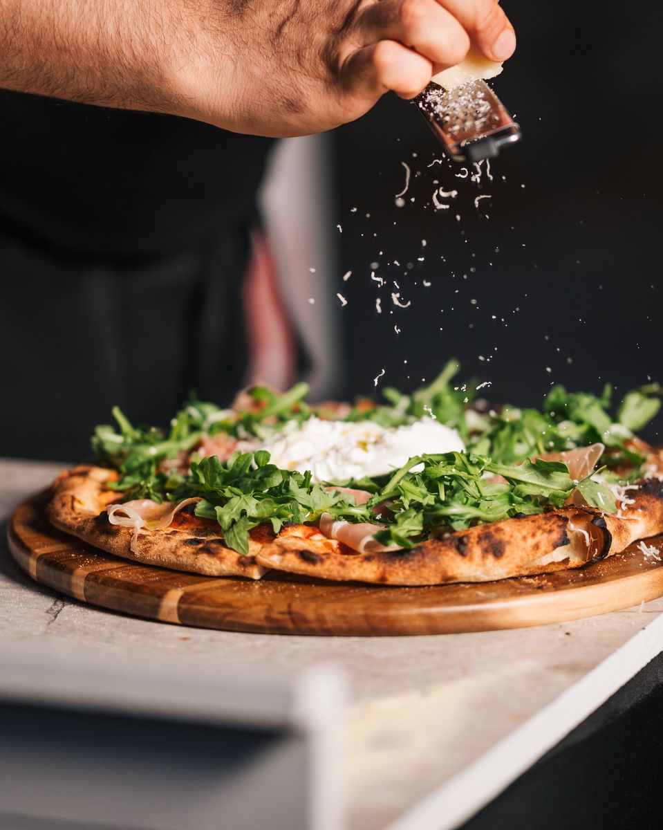 Chef finishing a pizza with freshly grated parmesan